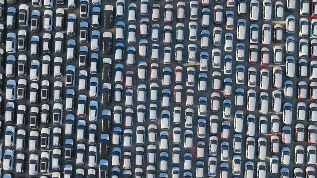 Thousands of new cars parked in perfect rows at a factory parking lot, an endless automotive background representing mass production, car dealership inventory, and the automotive industry