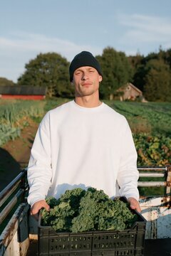 Young farmer holding crate of fresh kale on organic farm field for sustainable food background and agricultural banner design