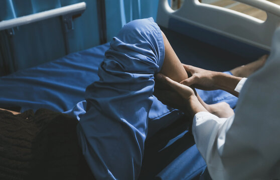 Asian male doctor examining foot of female patient sitting on bed in hospital room. Performing medical checkup. Diagnosing injury. Providing healthcare. Podiatry. Physical therapy. And rehabilitation