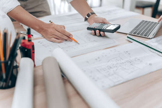 Creative professional working with architectural blueprints designs with tools and technology on office desk