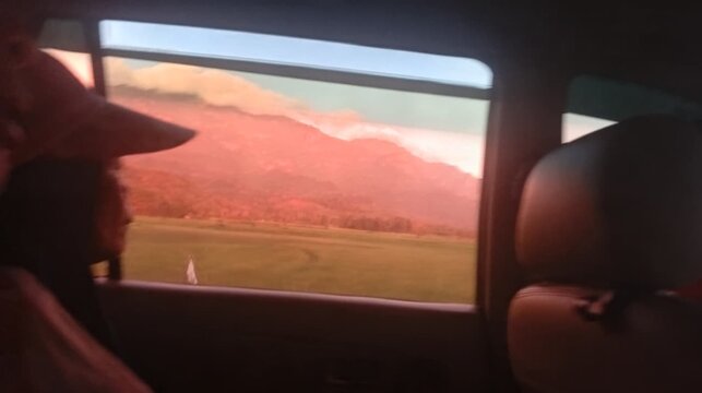 Passenger looking out the car window at a scenic mountain landscape during sunset. Motion blur view of mountains and fields from inside a moving vehicle.