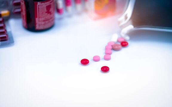 Red tablets pills on blurred background of tablets, stainless steel drug tray, and vitamin bottle. Pharmaceutical industry. Pharmacy drugstore products. Healthcare and medicine concept. Pharmaceutics.