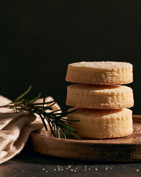 Shortbread Cookies Stacked On A Small Wooden Plate With A Rosemary Sprig And Linen Napkin. Moody Food Still Life For Bakery, Holiday, And Recipe Ese.