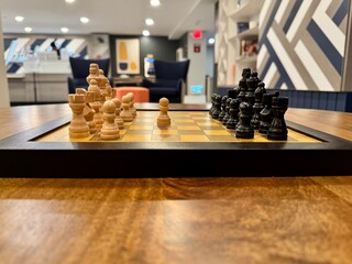 Chessboard with black and natural wood pieces arranged for play on a table in a modern indoor lounge with a softly blurred background. © Solomon Thompson