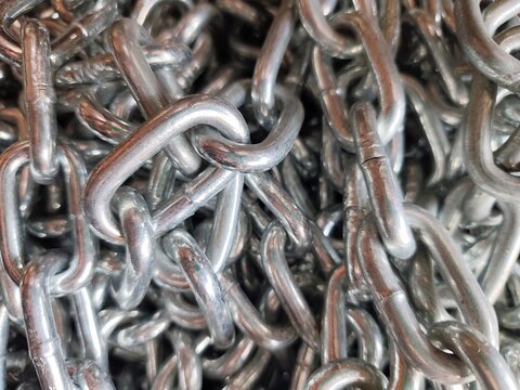 Close up view of shiny steel metallic chain links piled together creating a textured industrial background.   