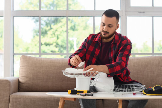 Home repair and maintenance, man fixing a broken electric fan in the living room to save money and improve household energy efficiency and comfort
