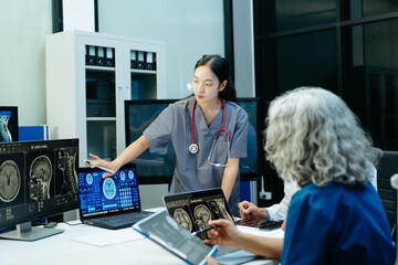 Asian female doctor in scrubs explains MRI brain scans to her medical team on a laptop in a modern...