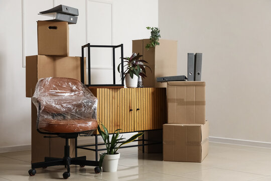 Cardboard boxes with chest of drawers and chair in rented office on moving day