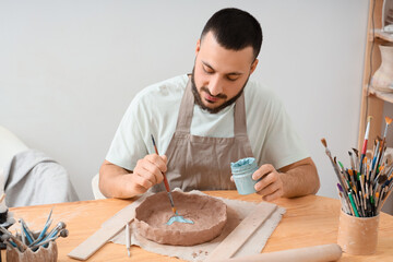 Craftsmanship and creative hobby, artisan potter painting clay bowl with blue glaze in workshop studio for handmade ceramics and small business production © Pixel-Shot
