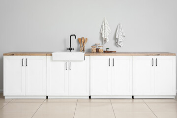 Interior of stylish kitchen with white counters, utensils and sink
