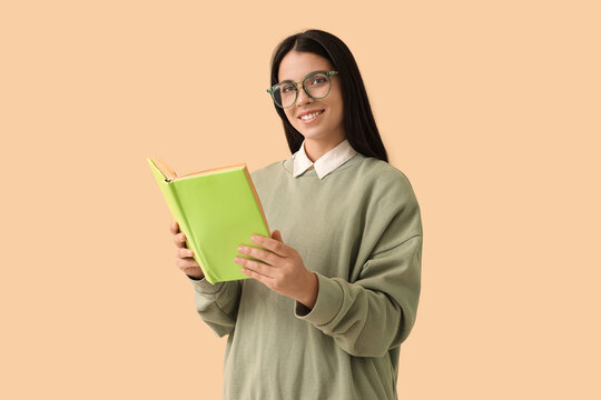 Beautiful woman in eyeglasses with book on beige background
