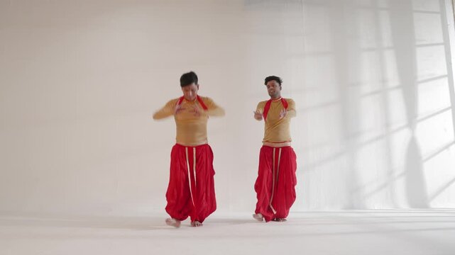 Two Indian male dancers are energetically performing traditional moves in a studio setting