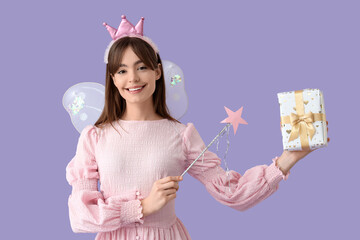 Fototapeta premium Young woman in fairy costume with wand and gift box on lilac background