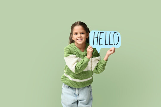 Cute little happy girl holding paper speech bubble with word HELLO on green background