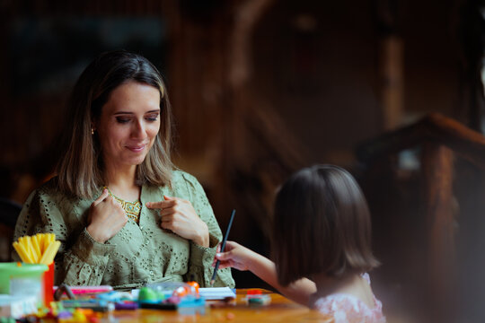 Curious Mother Wondering If Her Little Daughter Drew Her Portrait. Thoughtful smiling woman points at herself while watching her young child drawing at the table
