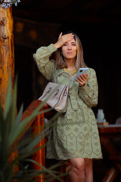 Worried Woman Checking Her Smartphone While Standing On Wooden Veranda. Anxious lady holds feels concerned looking at a mobile phone screen on a porch