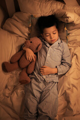 Obraz premium Cute little Asian boy in pajamas with toy bear sleeping in bed