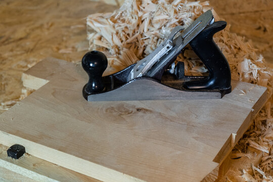 Traditional hand plane on a wooden board with wood shavings in a workshop