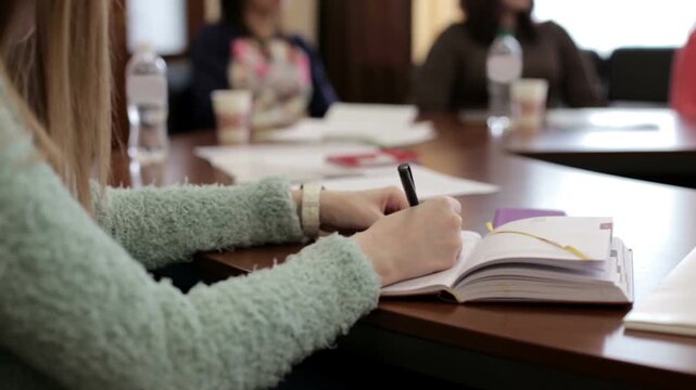 Close up female student hand writing notes in paper notebook using pen during exam or educational study at classroom