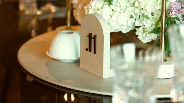 Arched wooden table number eleven stands on a round mirrored table beside white hydrangeas and a ceramic candle holder.