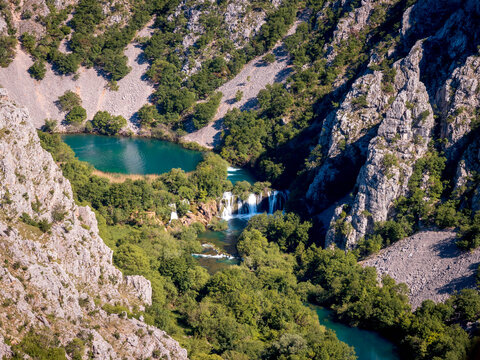 Elevated view of a hidden turquoise lake and waterfall in a rugged limestone canyon, Croatia   