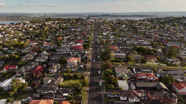 High aerial view of residential Mount Roskill suburbs at sunset, showing houses, streets, a tracking car and surrounding urban development in Auckland, New Zealand.