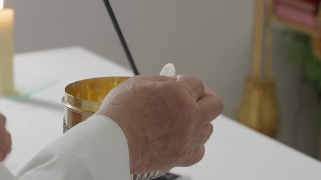 Hand raising eucharistic wafer at the altar with microphone candle and gilded altarpiece
