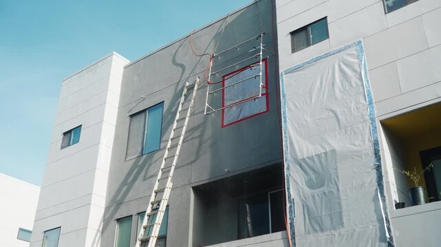A tall extension ladder and hose run up a building wall for a window water test