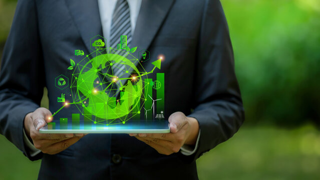 Businessman holding tablet with green glowing earth hologram outdoors. Represents ESG, carbon footprint reduction, climate action plan, green transition and sustainable corporate growth. Go green. CO2