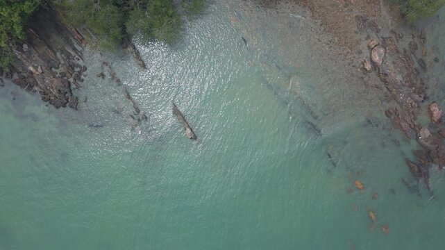 Aerial view (pull up shot) of a rocky and sandy beach with deep turquoise water