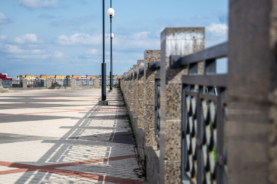 Sharp lines of metal railing fence cast distinct geometric shadows on paved public overpass under clouds with copy space