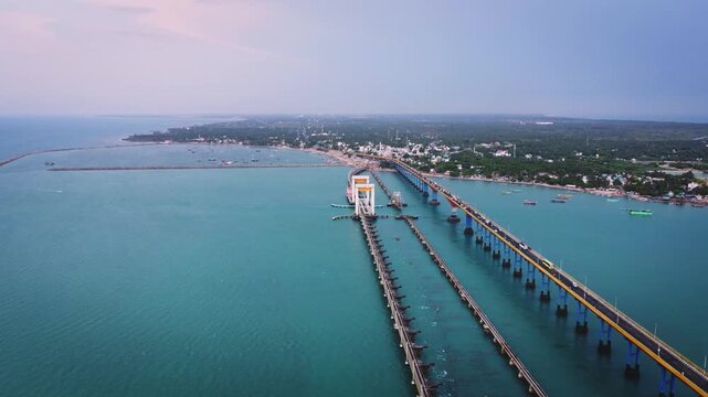 Aerial view of Pamban Bridge and the surrounding coastal landscape of Rameswaram Island, with railway tracks, turquoise sea, boats, and the shoreline of Tamil Nadu.