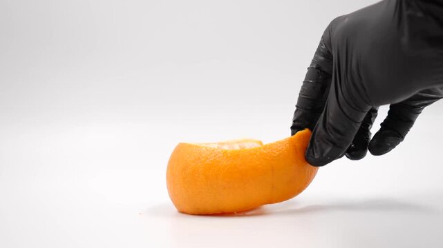 Peeled fresh orange segment held in an open human hand palm with a black gloved hand holds an orange on a white background