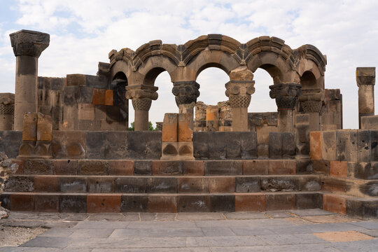 Historic stone arches and columns of Zvartnots Cathedral, showcasing ancient Armenian architecture under a cloudy sky.
