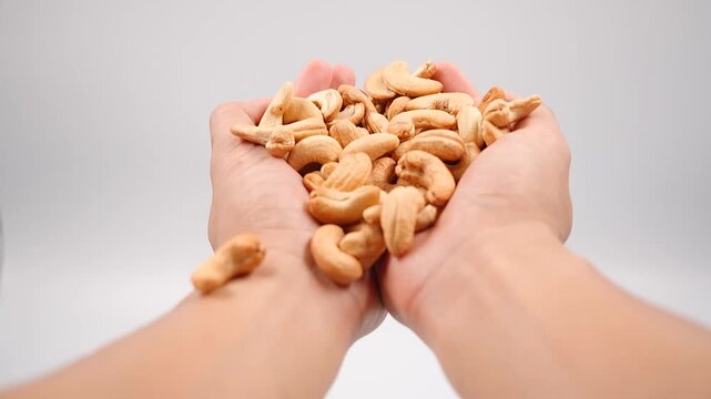 man holding cashew nuts  Hand reaching into cashew pile isolated on a white background. A human hand reaches into a pile of cashew nuts on a white background.