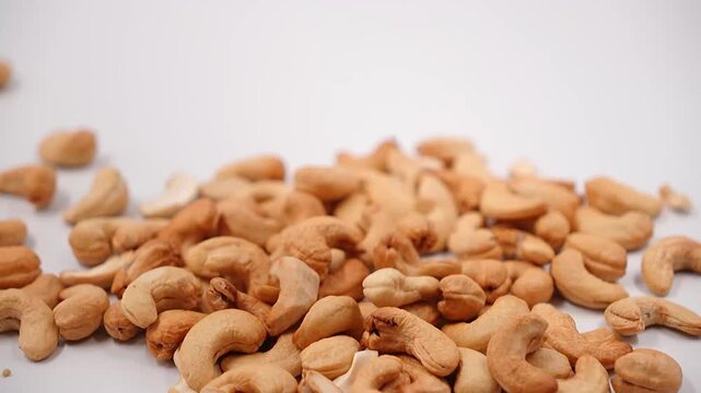 Peeled cashew nuts falling onto a heap on white background.  Cashews pile up, perfect for natural snacks, cooking, healthy eating concepts.