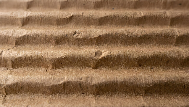 Corrugated cardboard surface featuring rough paper textures and warm brown horizontal lines.