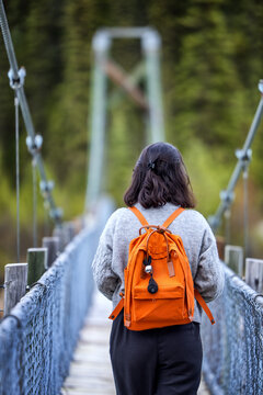 Woman with an orange backpack walks on a suspension bridge