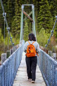 Woman with orange backpack walking on a suspension bridge