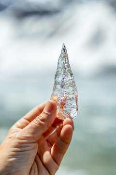 Woman's hand holding a clear piece of ice against a blurred lake