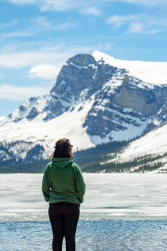 Woman stands looking at Bow frozen lake with snow capped mountains