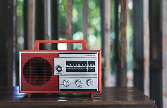Old red radio with a classic vintage look sits on wooden table at home, space for text, against blurred background.