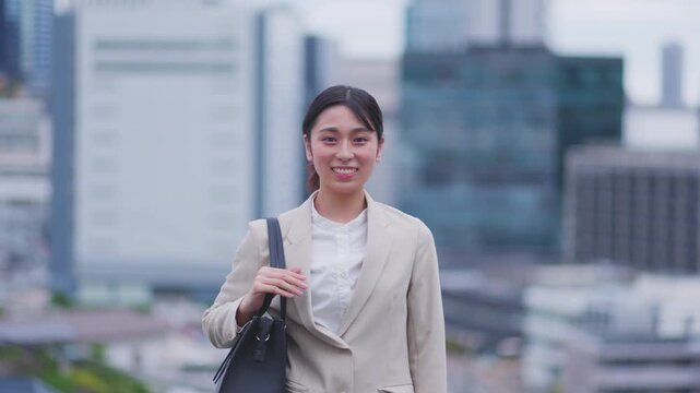 ビル街を背景にカメラへ微笑むスーツ姿の女性 スローモーション
