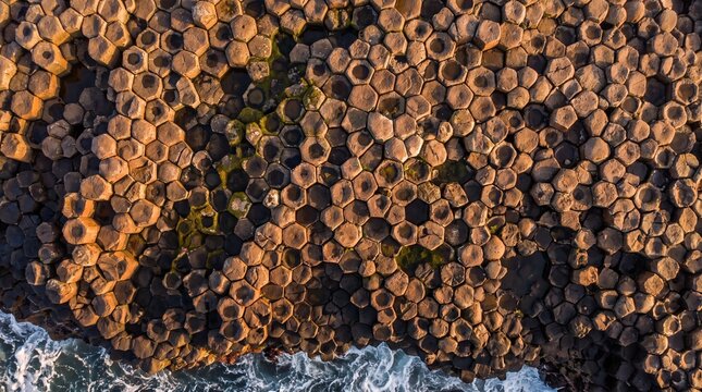 Hexagonal basalt columns formation aerial top down view showing intricate geometric rock patterns along the coastline with crashing ocean waves creating natural coastal geological wonder