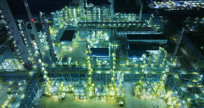 Illuminated chemical refinery and industrial plant at night, showing complex pipelines, distillation columns, and modern engineering infrastructure.
