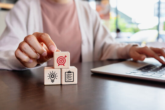 A female business professional hand places a wooden block featuring a target symbol, representing business planning, goal setting and strategic planning.
