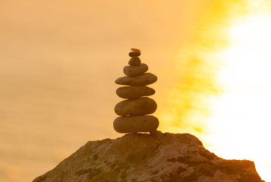 Stacked balance stones on a rocky peak at sunset, glowing in warm golden light. Minimalist nature scene symbolizing balance, harmony and tranquility.