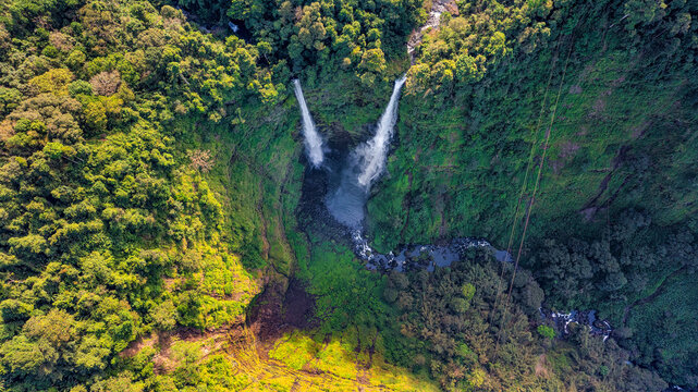 Aerial view of Tad Fane Waterfall in Laos, with a tourist enjoying tea while suspended on a zipline above the spectacular twin cascades and lush rainforest of the Bolaven Plateau.