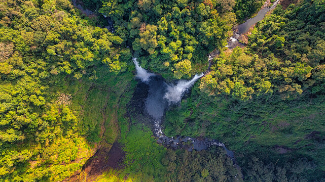 Aerial view of Tad Fane Waterfall in Laos, with a tourist enjoying tea while suspended on a zipline above the spectacular twin cascades and lush rainforest of the Bolaven Plateau.