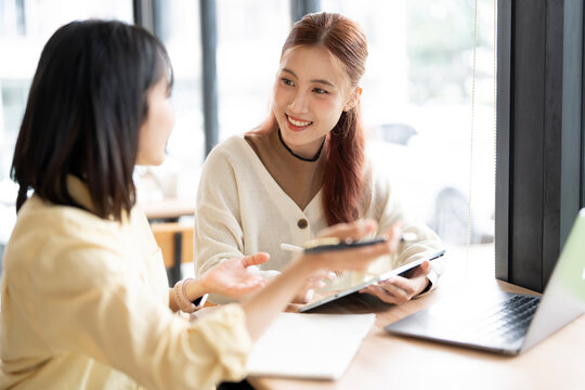 Asian Business Women Smiling and Discussing Project with Notebook and Laptop

Description